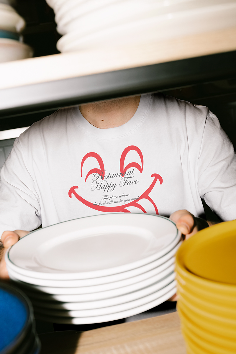 Restaurant Happy Face staff wearing branded T-shirt with smiley face logo while stacking white plates in kitchen